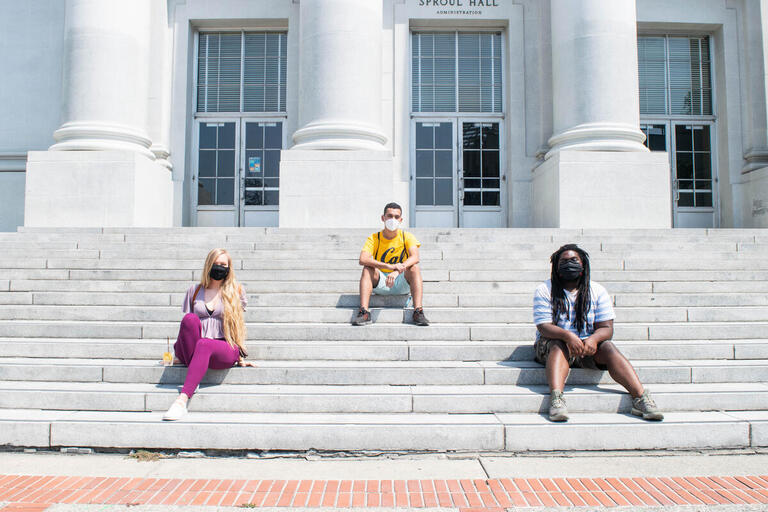 Berkeley students with face coverings sitting on Sproul Hall steps