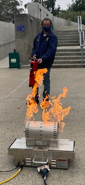 ehs team member using fire extinguisher on live fire prop